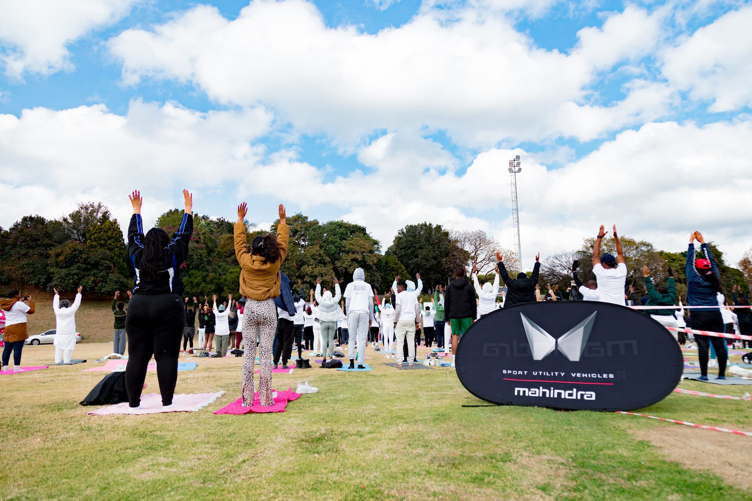 Community members practicing yoga on mats at Randburg Cricket Club with a Mahindra banner nearby