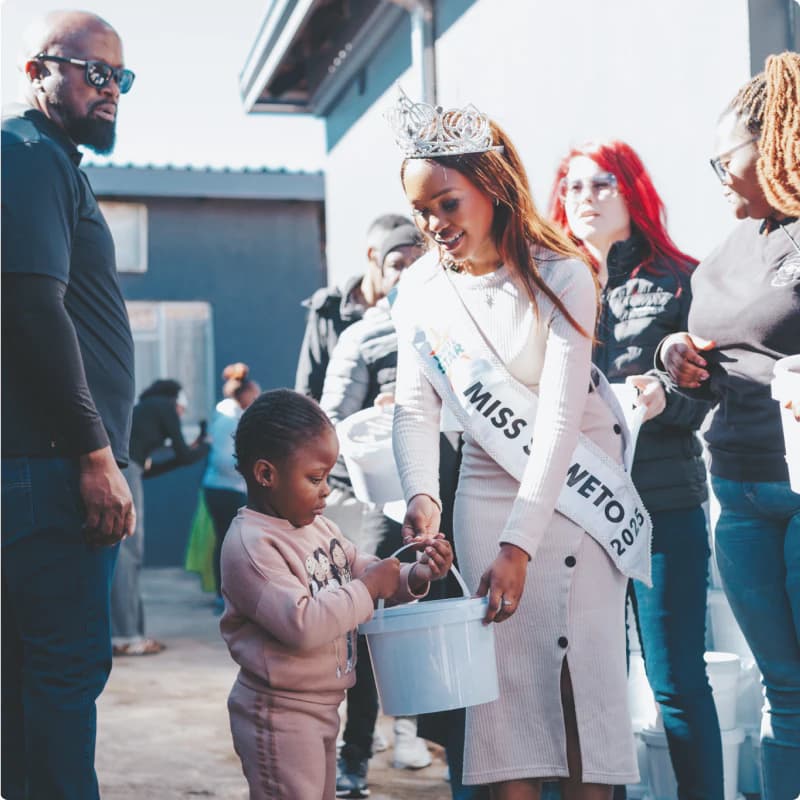 Miss Soweto presenting a donation bucket to a child during Mandela Day outreach